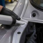 Nakładanie kleju na łączenie elementów karoserii samochodu srebrnym pistoletem dozującym