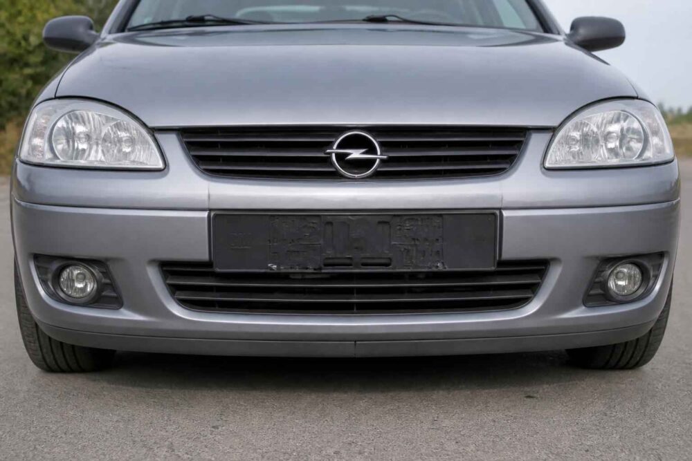 Srebrny Opel widziany z przodu, z widocznym grillem, reflektorami i tablicą rejestracyjną