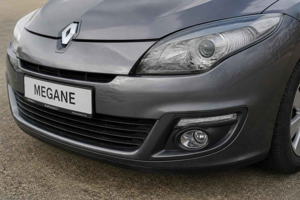 Przedni fragment szarego Renault Megane z reflektorem, atrapą chłodnicy i tablicą Megane