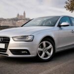 Srebrne Audi A4 zaparkowane przy nabrzeżu, z panoramą miasta w tle
