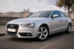 Srebrne Audi A4 zaparkowane przy nabrzeżu, z panoramą miasta w tle
