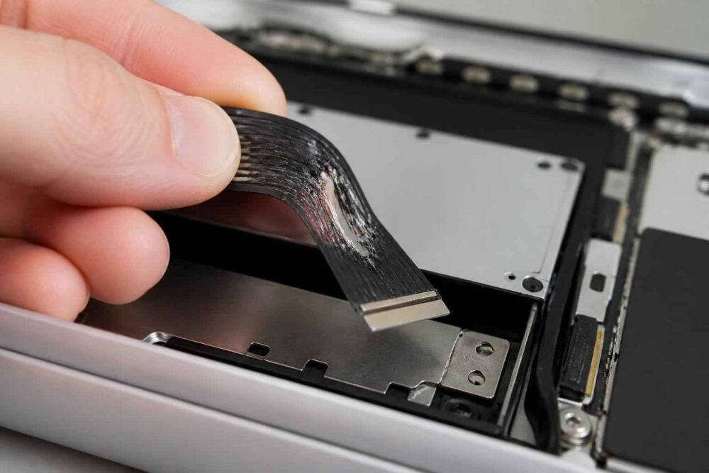 Dłoń podnosi elastyczną taśmę połączeniową wewnątrz rozebranego urządzenia elektronicznego